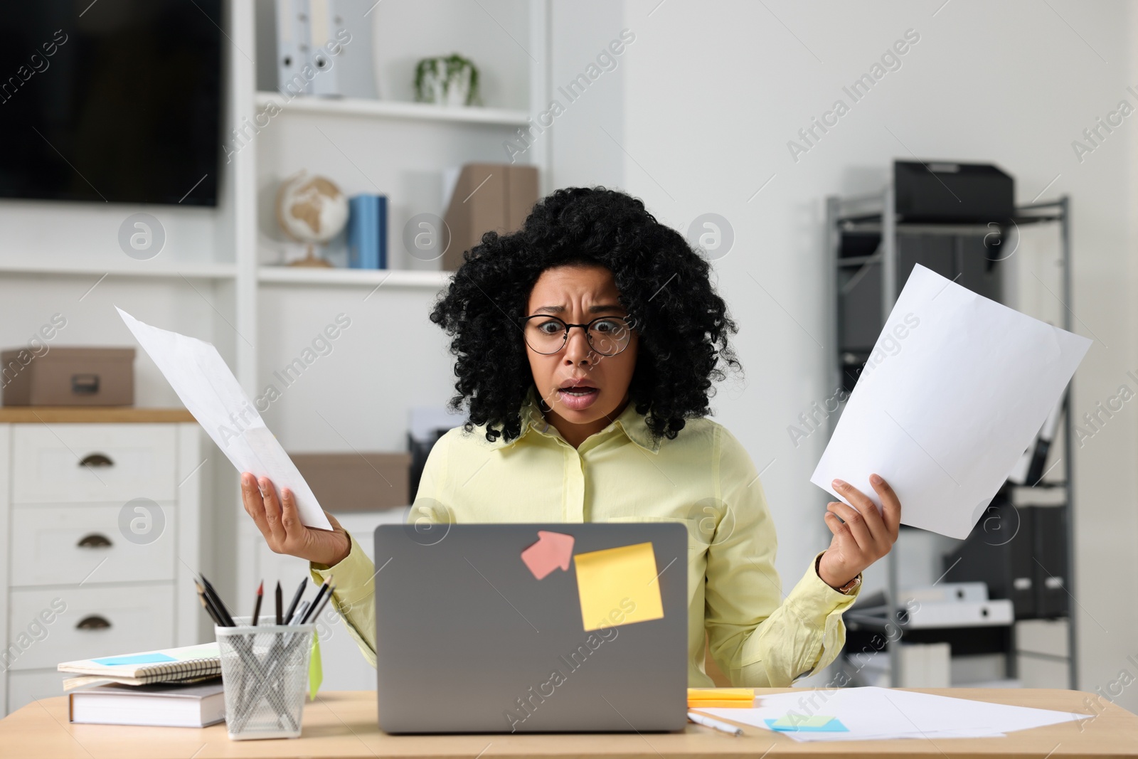 Photo of Deadline concept. Scared woman holding documents and looking at laptop in office