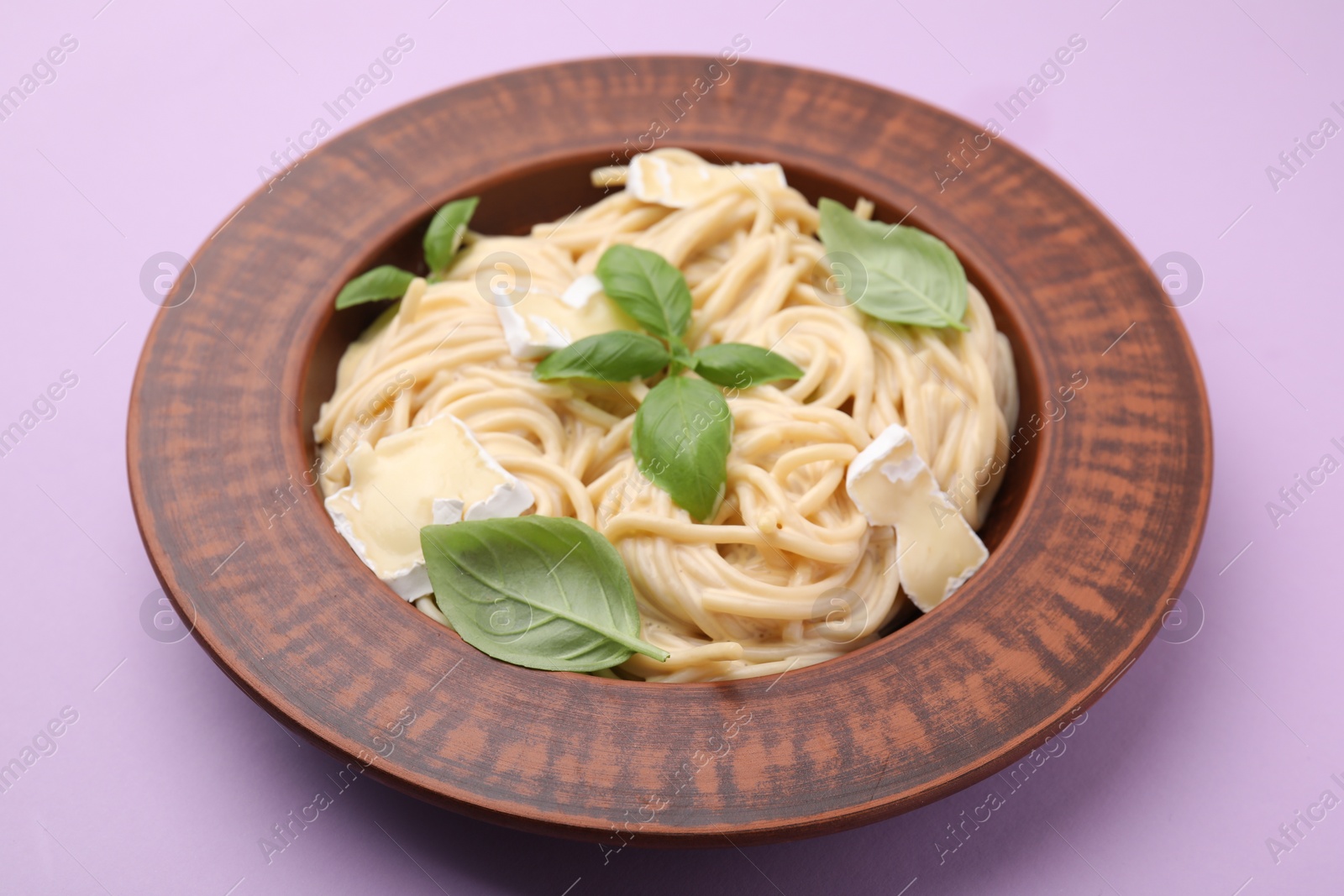 Photo of Delicious pasta with brie cheese and basil leaves on violet table, closeup