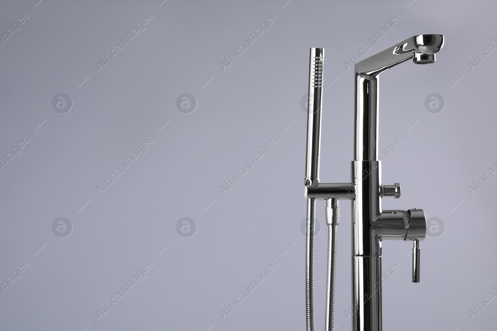 Photo of Modern bathtub faucet with hand shower on grey background. Space for text