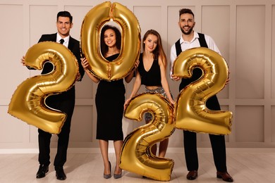 Photo of Happy friends with golden 2022 balloons indoors. New Year celebration