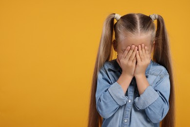 Photo of Resentful girl covering her face with hands on orange background. Space for text