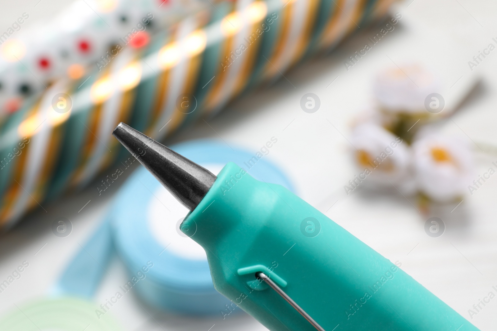 Photo of Hot glue gun over table with handicraft materials, closeup