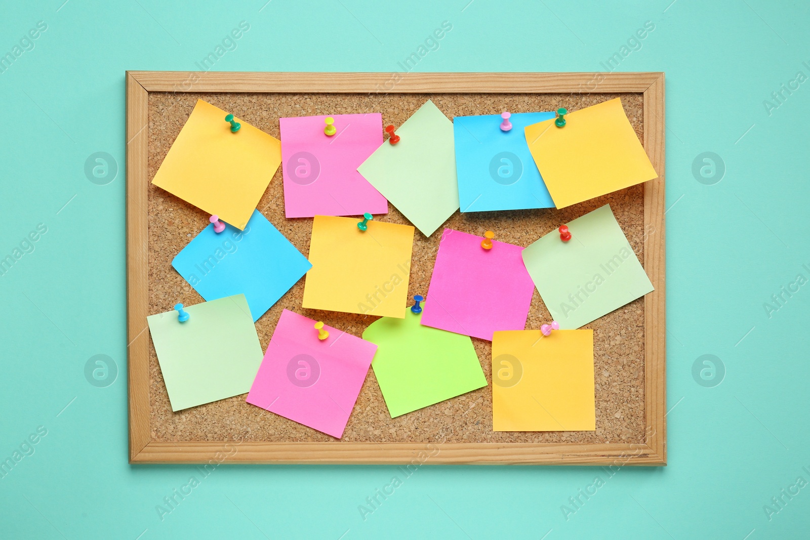 Photo of Many blank colorful notes pinned to corkboard on turquoise background, top view. Space for text