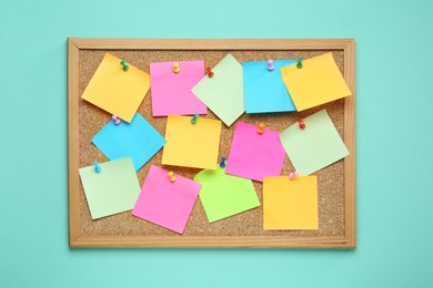 Photo of Many blank colorful notes pinned to corkboard on turquoise background, top view. Space for text