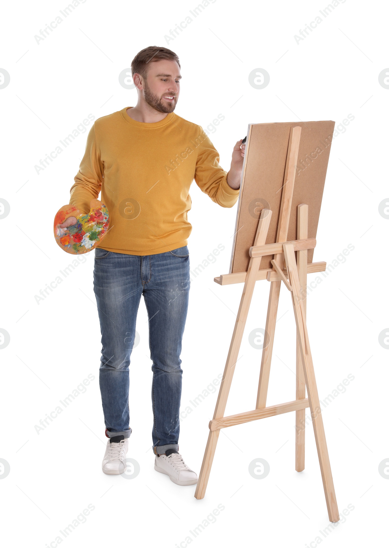 Photo of Man painting with brush on easel against white background. Young artist