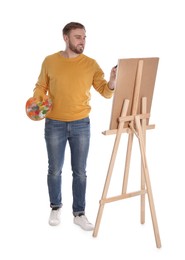 Man painting with brush on easel against white background. Young artist