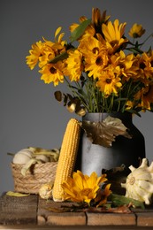 Beautiful autumn bouquet, small pumpkins and corn cobs on wooden table against grey background