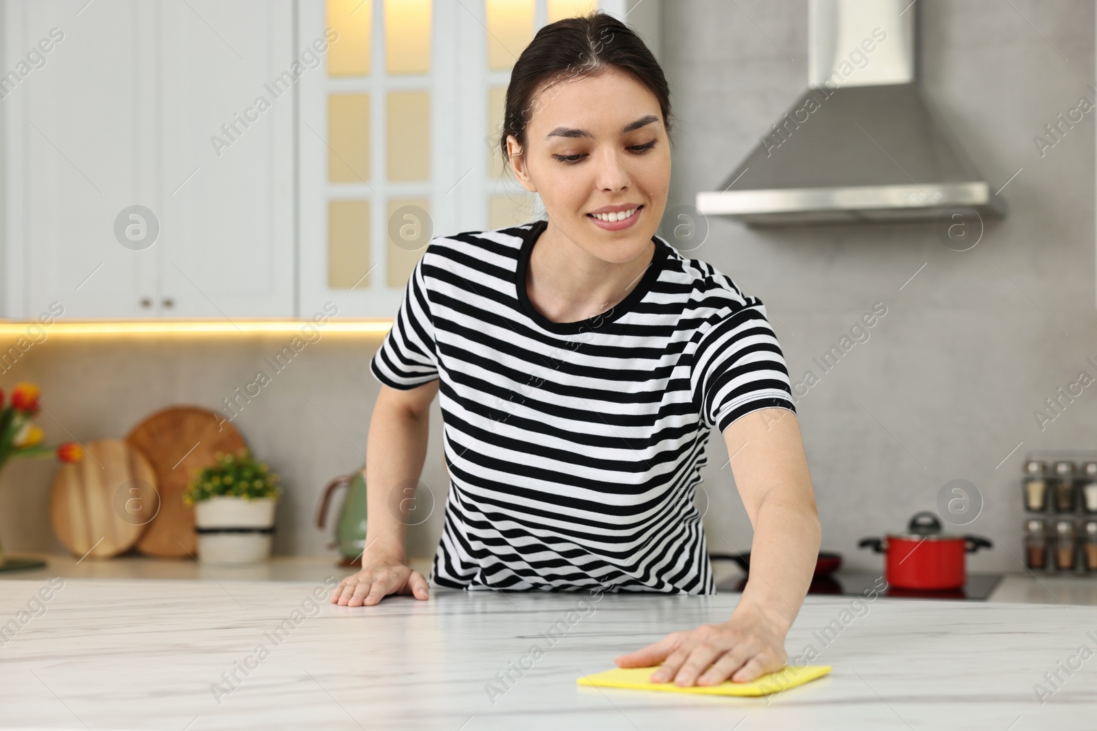 Photo of Woman cleaning countertop with sponge wipe in kitchen