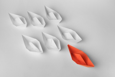 Photo of Group of paper boats following orange one on white background, above view. Leadership concept