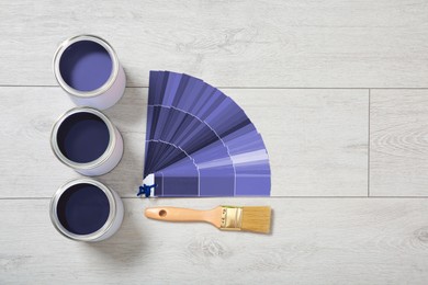 Cans of violet paints, color palette samples and brush on wooden background, flat lay