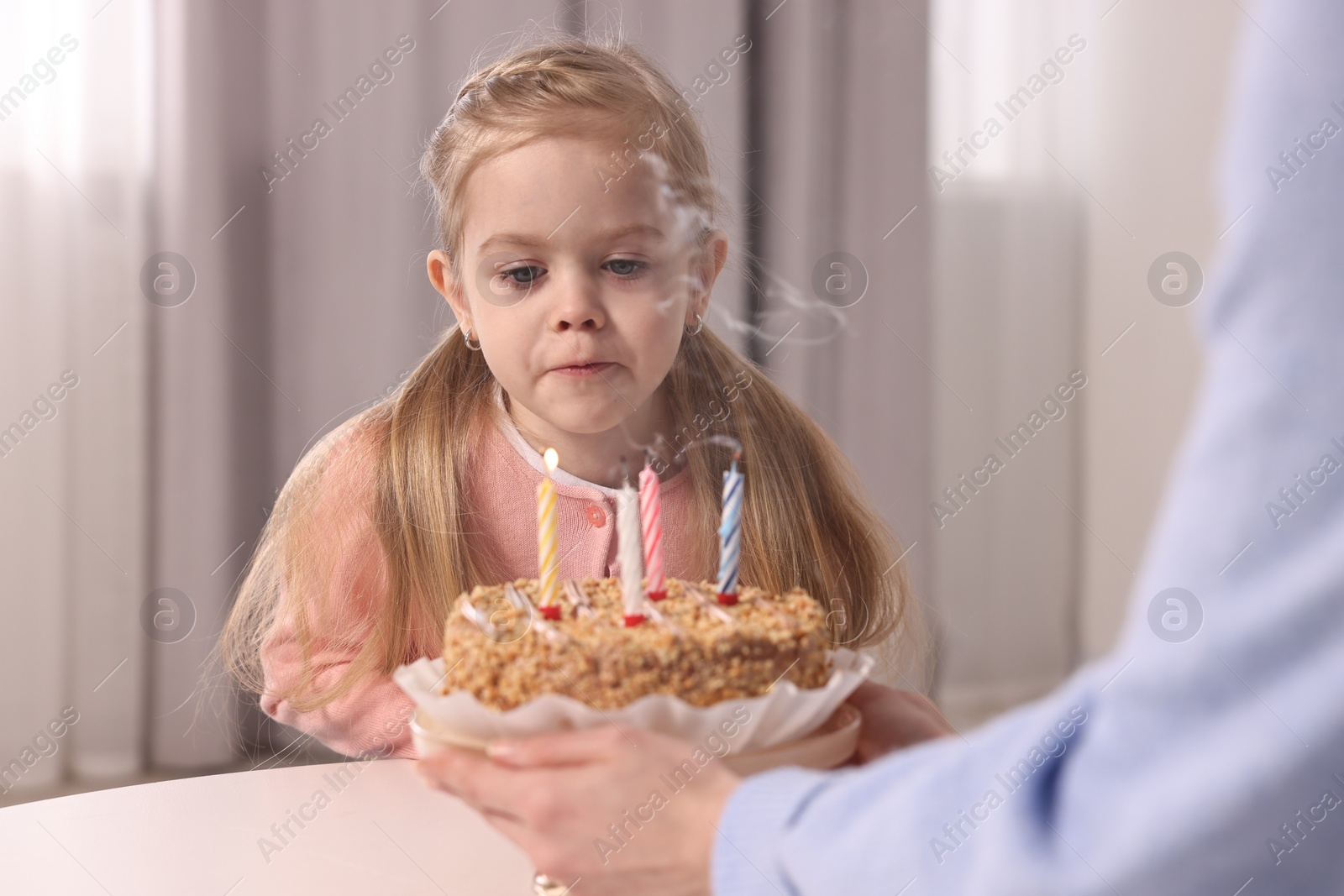 Photo of Birthday celebration. Mother holding tasty cake with burning candles near her daughter indoors