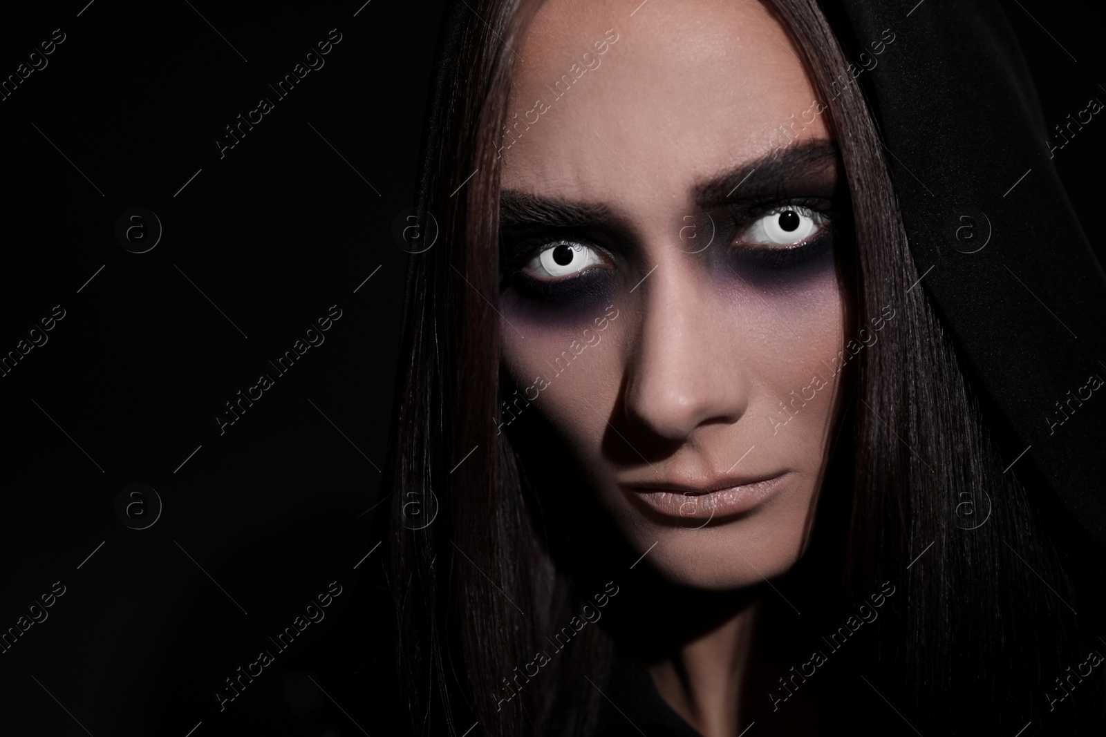 Photo of Mysterious witch with spooky eyes on black background, closeup