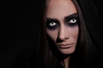 Photo of Mysterious witch with spooky eyes on black background, closeup