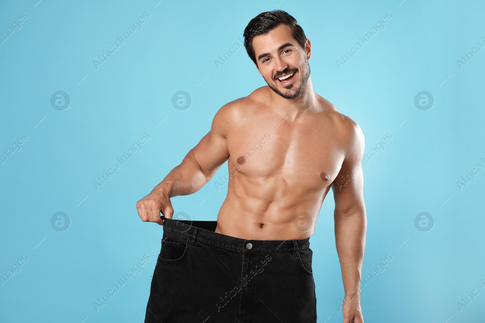 Photo of Young man with slim body in old big size jeans on light blue background