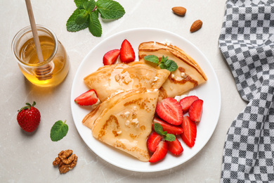 Delicious thin pancakes with strawberries, cottage cheese and honey on light table, flat lay