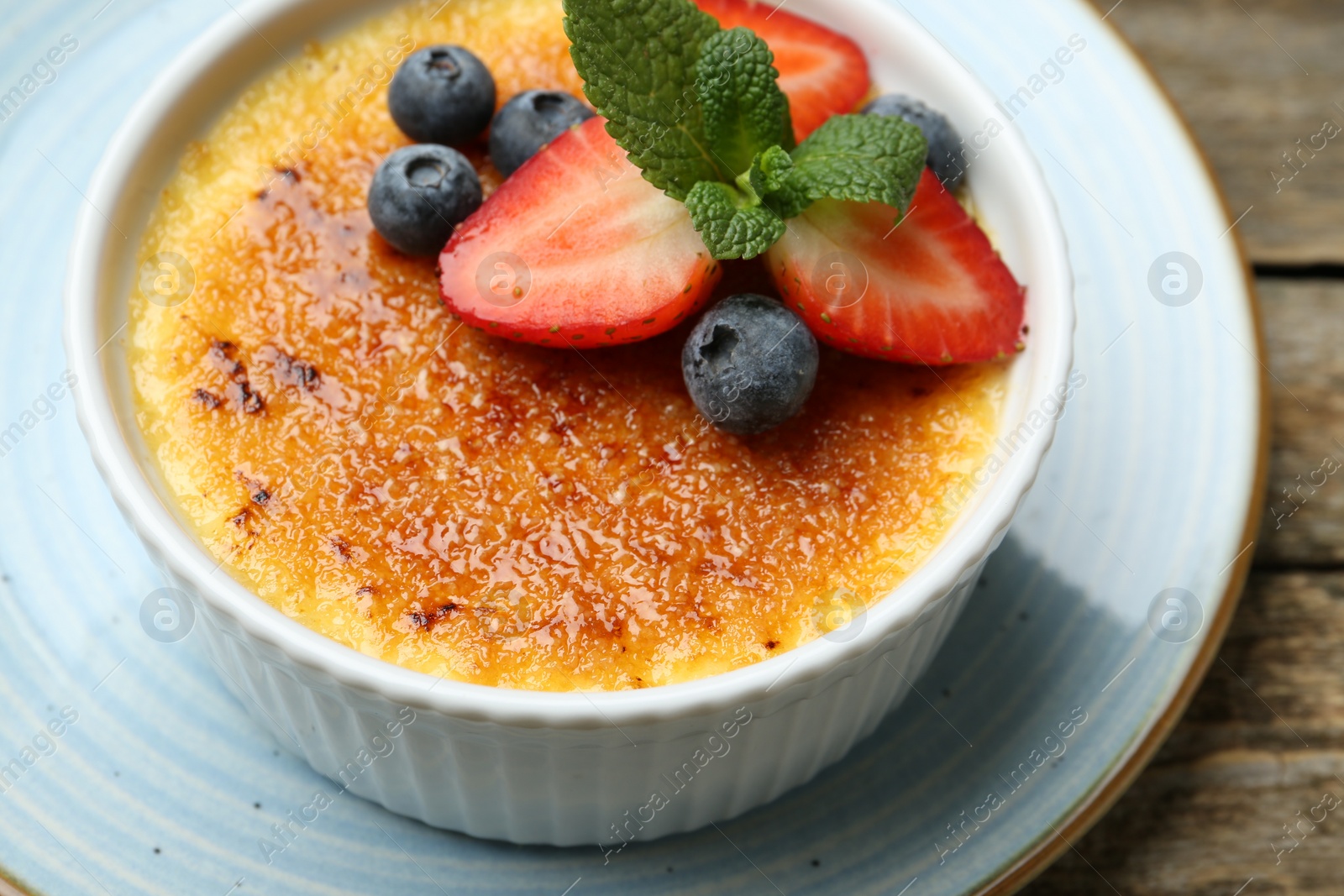 Photo of Delicious creme brulee with berries and mint in bowl on wooden table, closeup