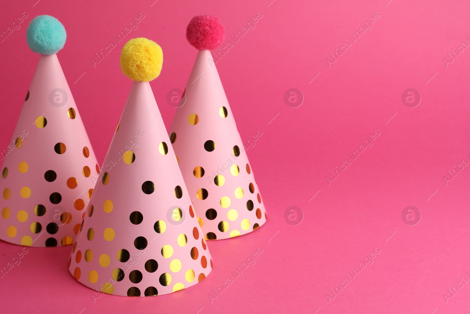 Photo of Beautiful party hats with pompoms on pink background, space for text