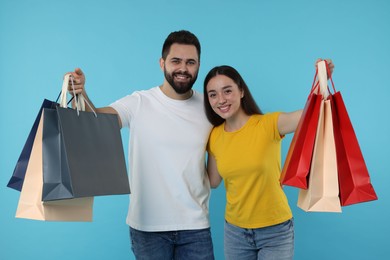 Happy couple with shopping bags on light blue background