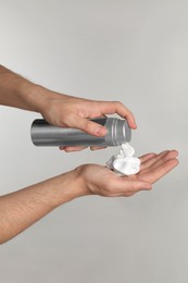 Photo of Man applying shaving foam onto hand on light grey background, closeup