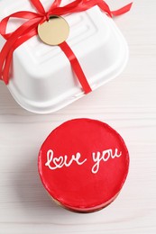 Photo of Bento cake with text Love You and takeaway packaging on white wooden table, flat lay. St. Valentine's day surprise