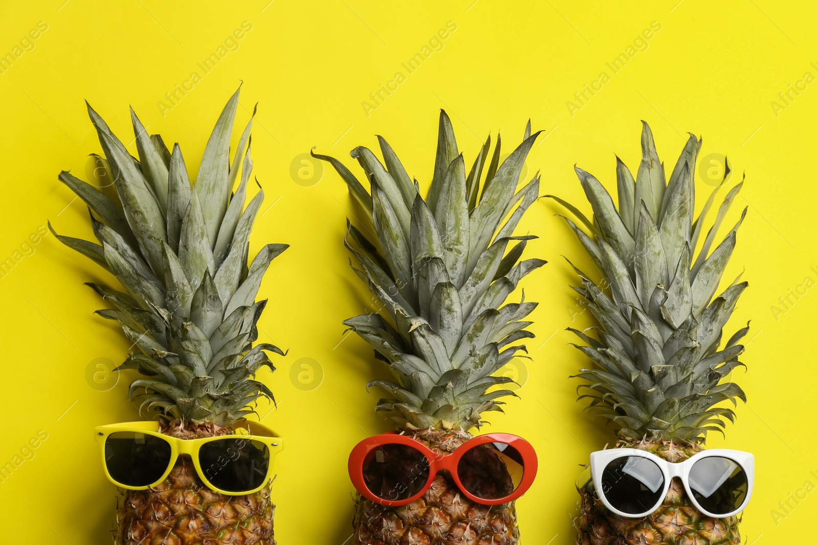 Photo of Pineapples with sunglasses on yellow background, flat lay. Creative concept