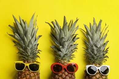 Photo of Pineapples with sunglasses on yellow background, flat lay. Creative concept