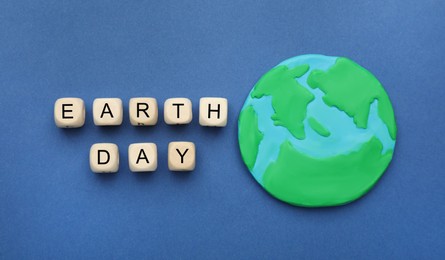 Photo of Phrase Earth Day made with wooden cubes and planet model on blue background, flat lay