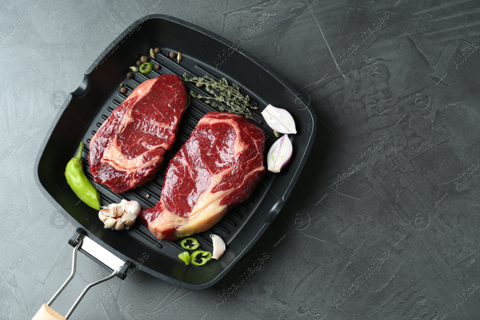 Photo of Grill pan with pieces of fresh beef meat, thyme and spices on gray table, top view. Space for text