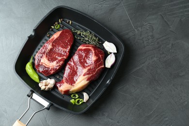 Grill pan with pieces of fresh beef meat, thyme and spices on gray table, top view. Space for text