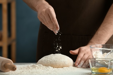 Photo of Man sprinkling flour over dough on table in kitchen