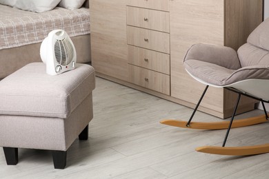 Photo of Modern electric fan heater on pouf in cozy room