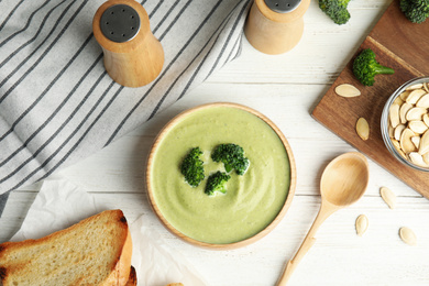 Photo of Delicious broccoli cream soup served on white wooden table, flat lay
