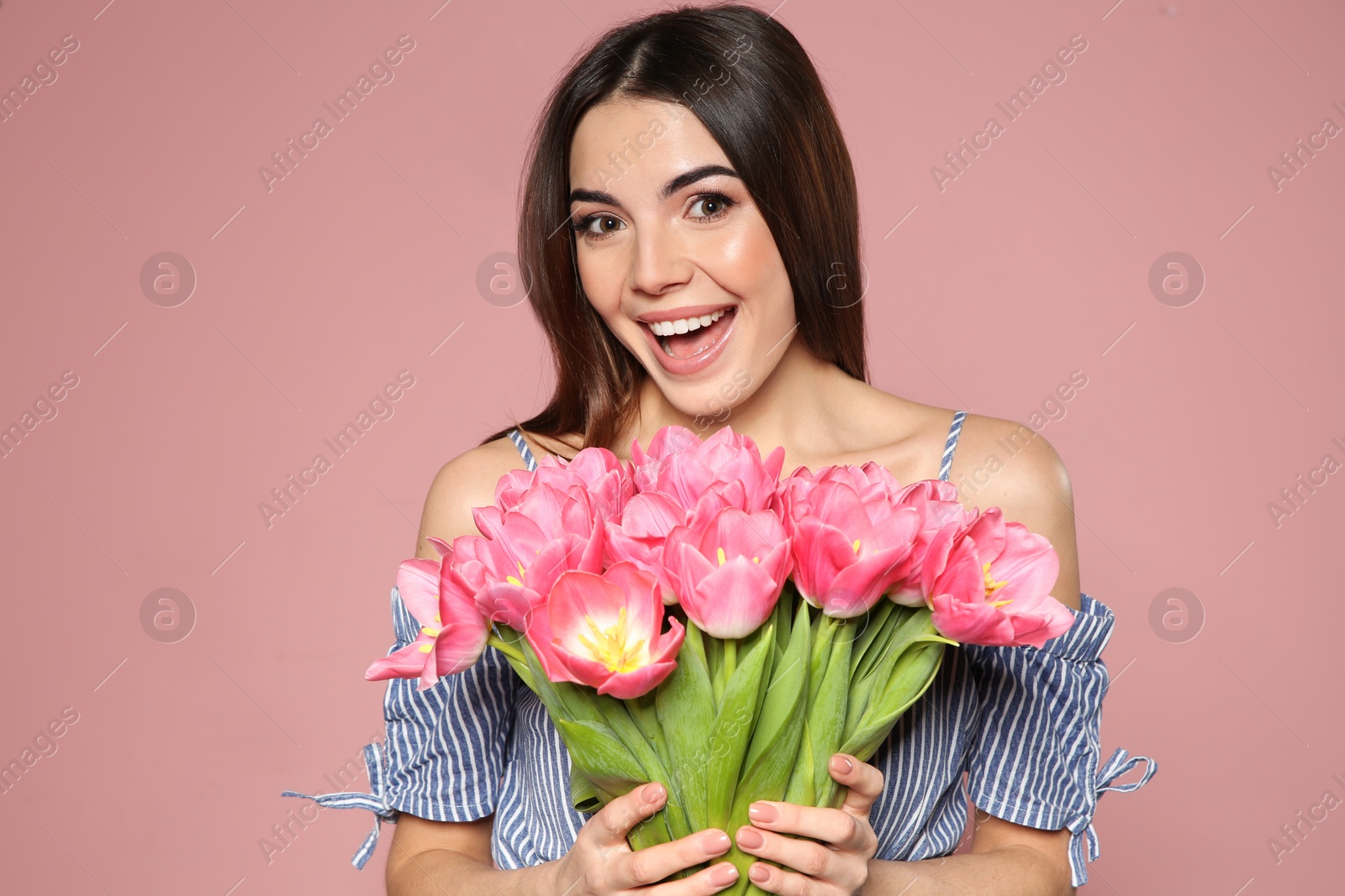 Photo of Portrait of beautiful smiling girl with spring tulips on pink background. International Women's Day