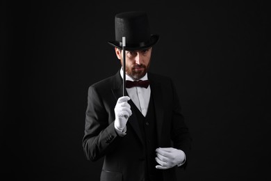 Photo of Magician in top hat holding wand on black background
