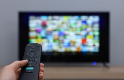 Photo of Woman switching channels on TV set with remote control at home, closeup. Space for text