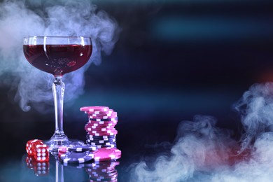 Image of Casino chips, dice and glass of wine on dark background with smoke. Space for text