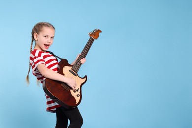 Photo of Cute girl with electric guitar on light blue background. Space for text