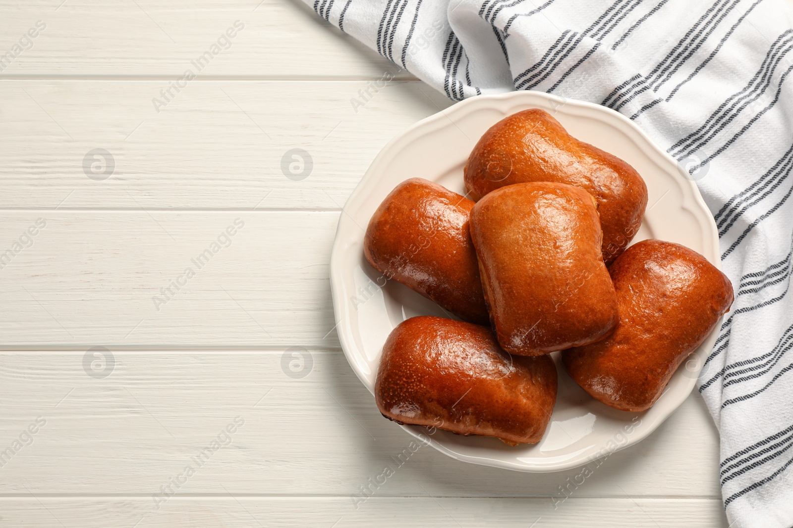 Photo of Delicious baked pirozhki on white wooden table, top view. Space for text