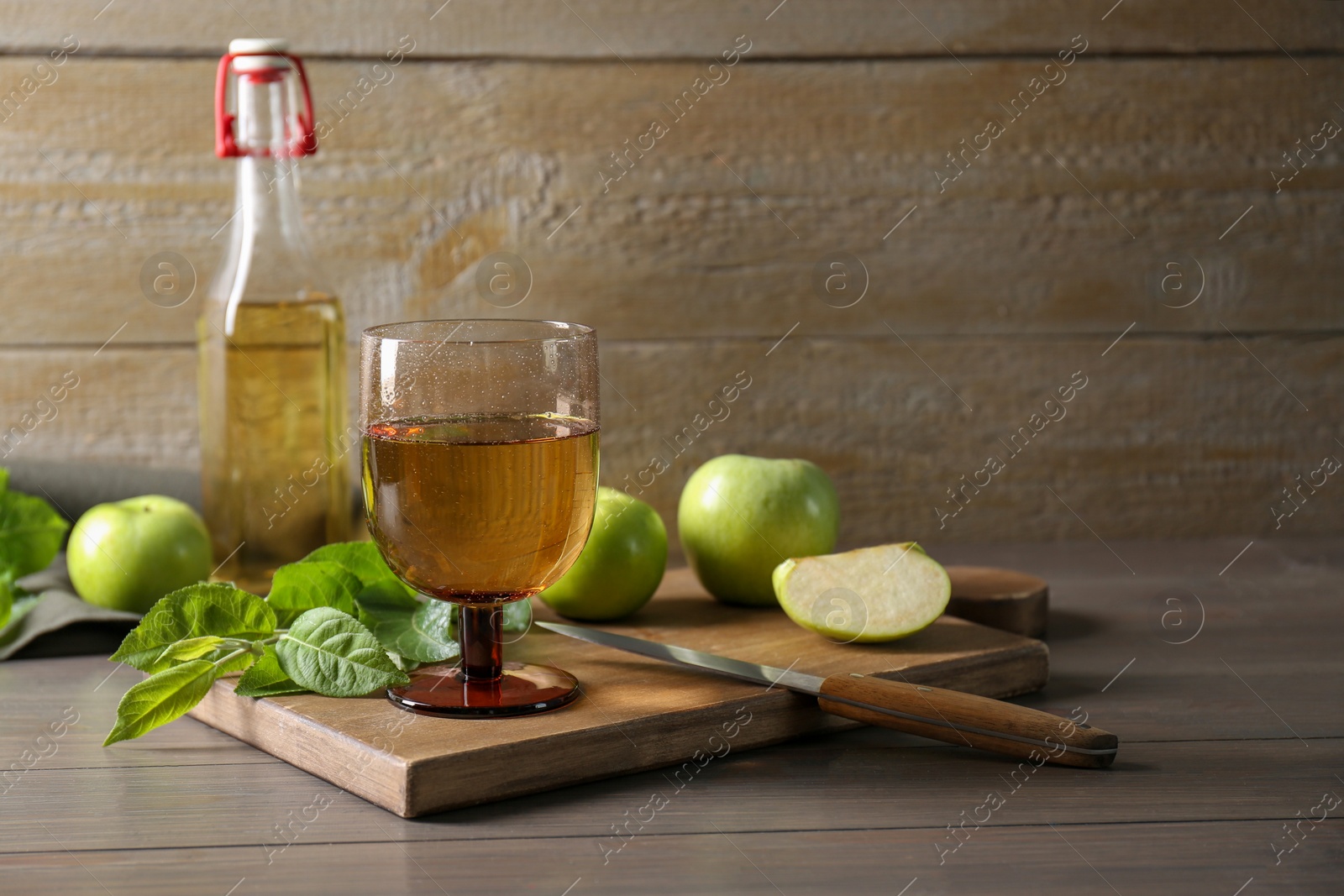 Photo of Delicious cider and apples with green leaves on wooden table, space for text