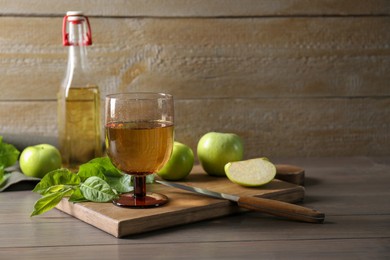 Photo of Delicious cider and apples with green leaves on wooden table, space for text