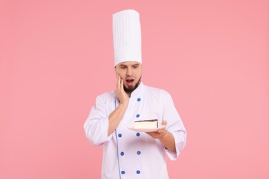 Photo of Surprised professional confectioner in uniform holding delicious cheesecake on pink background