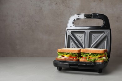 Modern grill maker with tasty sandwiches on light grey table. Space for text