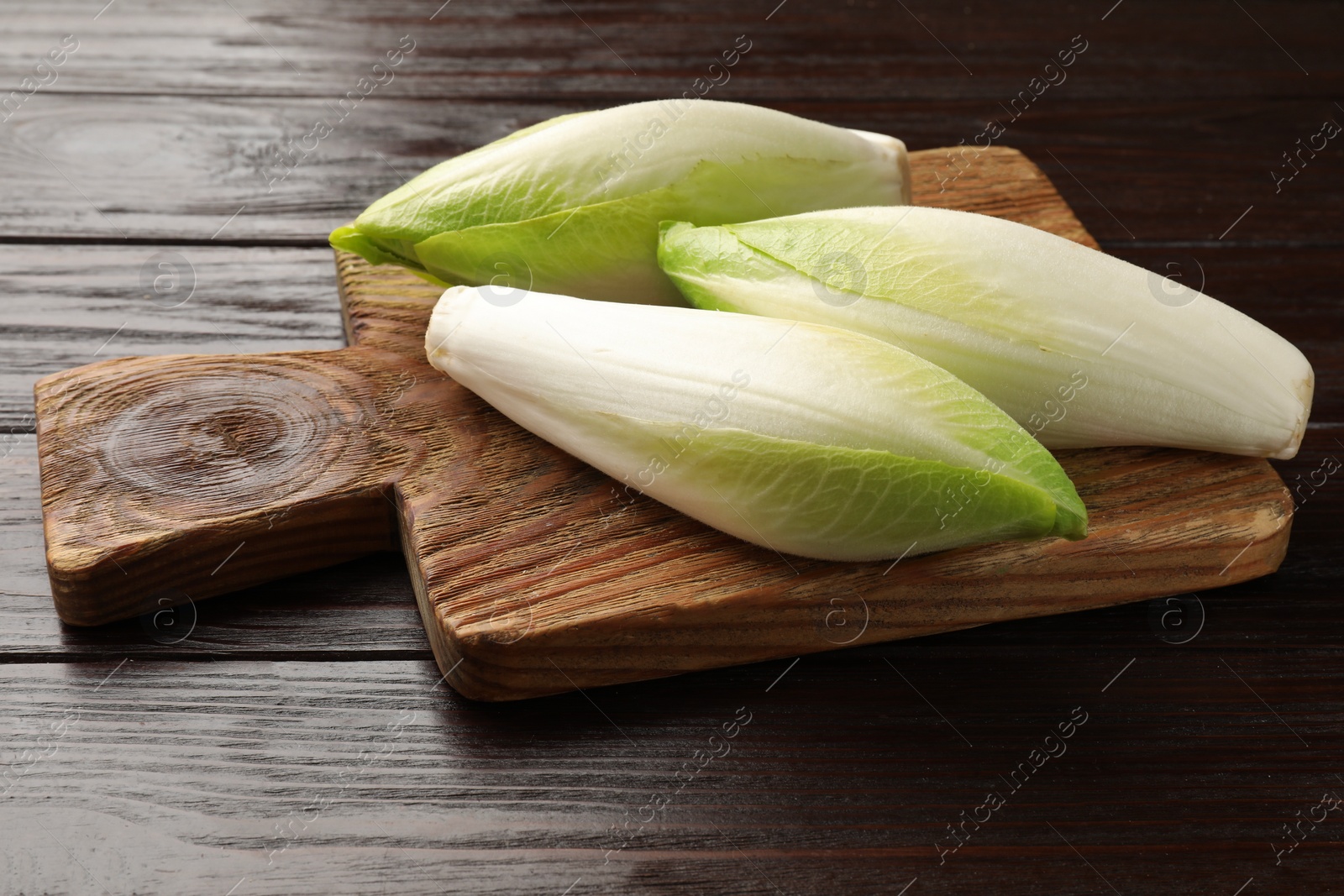 Photo of Board with raw ripe chicories on wooden table