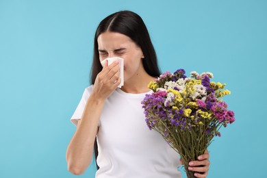 Photo of Suffering from allergy. Young woman with bouquet of flowers blowing her nose in tissue on light blue background