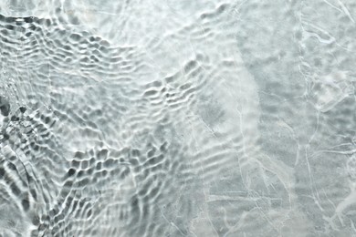 Rippled surface of clear water on light grey textured background, top view