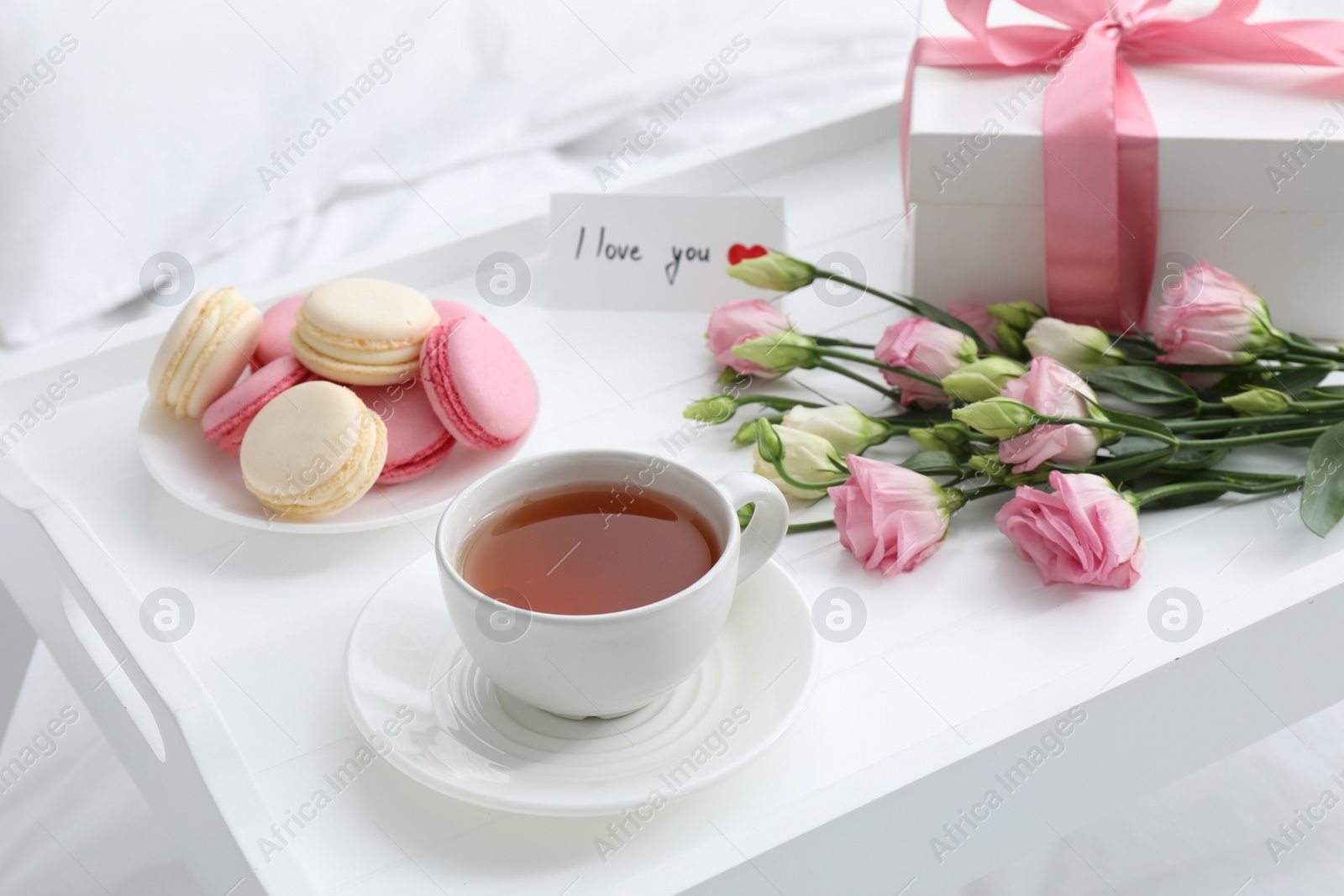 Photo of Tasty breakfast served in bed. Delicious macarons, tea, gift box, flowers and I Love You card on tray