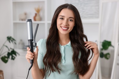 Happy woman with curling hair iron at home