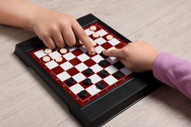 Photo of Children playing checkers at light wooden table, closeup