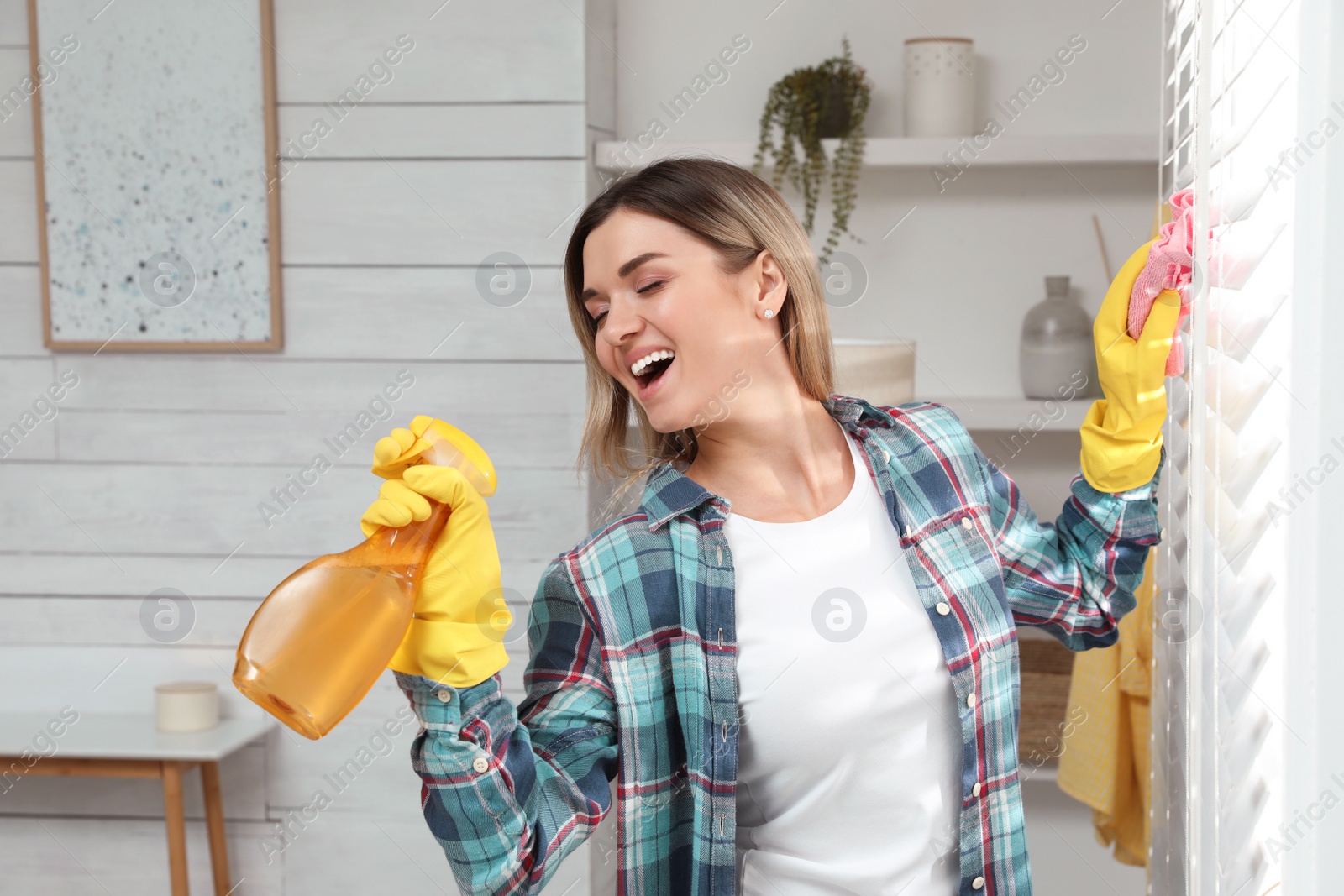 Photo of Woman with spray bottle and rag singing while cleaning at home