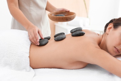 Photo of Beautiful young woman getting hot stone massage in spa salon